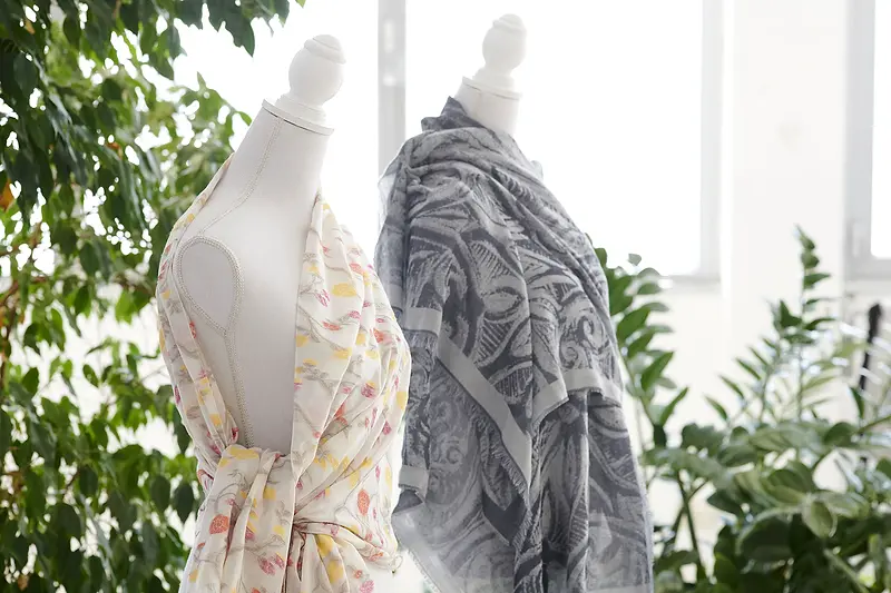 Due manichini con sciarpe jacquard, una a fiori chiari e una a disegni grigi, fra le piante