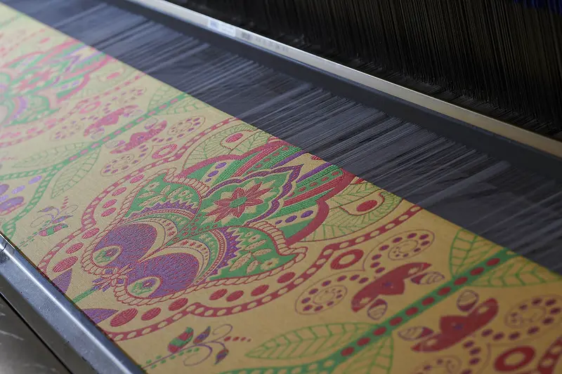 Un jacquard viola, verde e oro sul telaio, con i fili dell’ordito tesi sopra